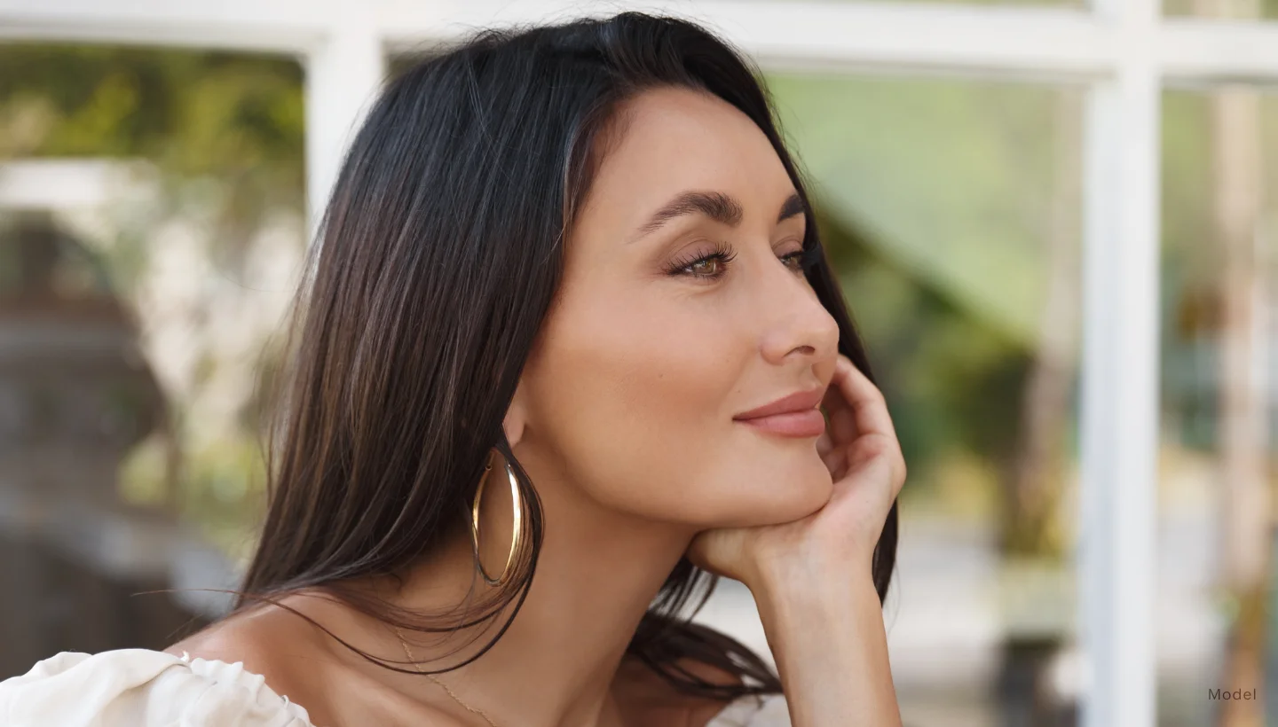 A woman with long black hair with full lips sitting with her face resting on her hand