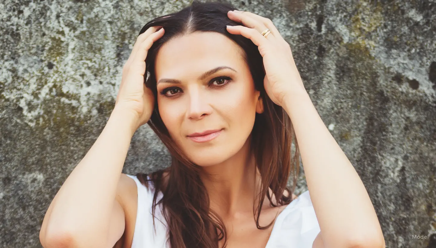 A woman who is wearing a white top and is sweeping her hair away from her face